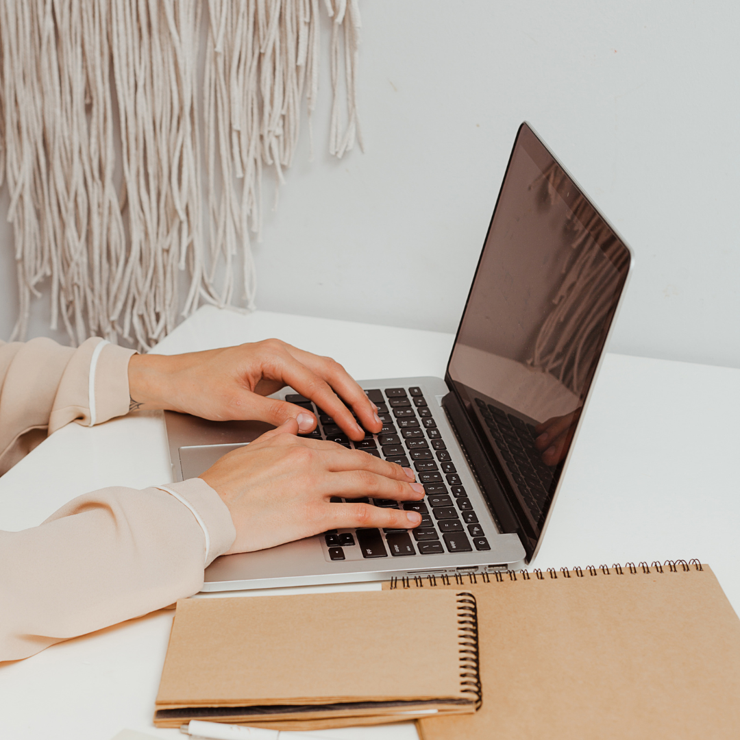 Person typing on a laptop with notebooks on a desk