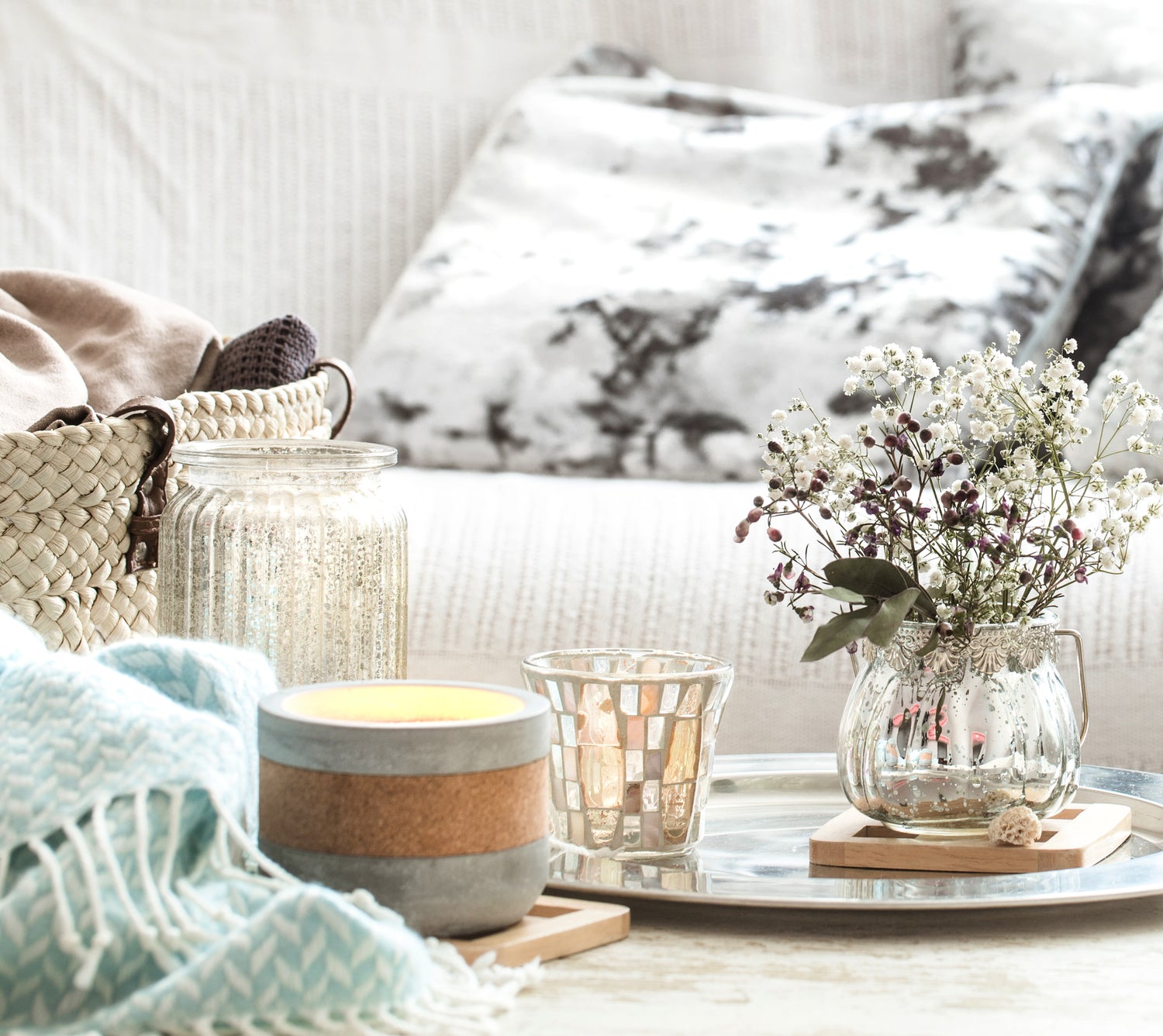 Cozy living room setting with candles, a vase of flowers, and a blanket on a couch.