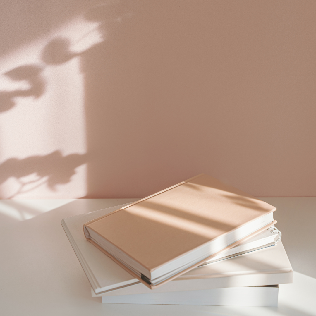 Stack of books on a light surface with a soft pink background