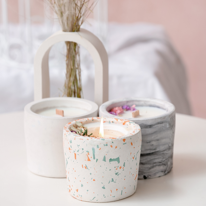 Three candles in decorative containers on a light surface with a blurred background