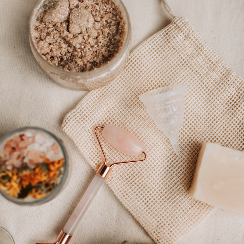 Skincare tools including a roller and a jar of scrub on a textured surface.