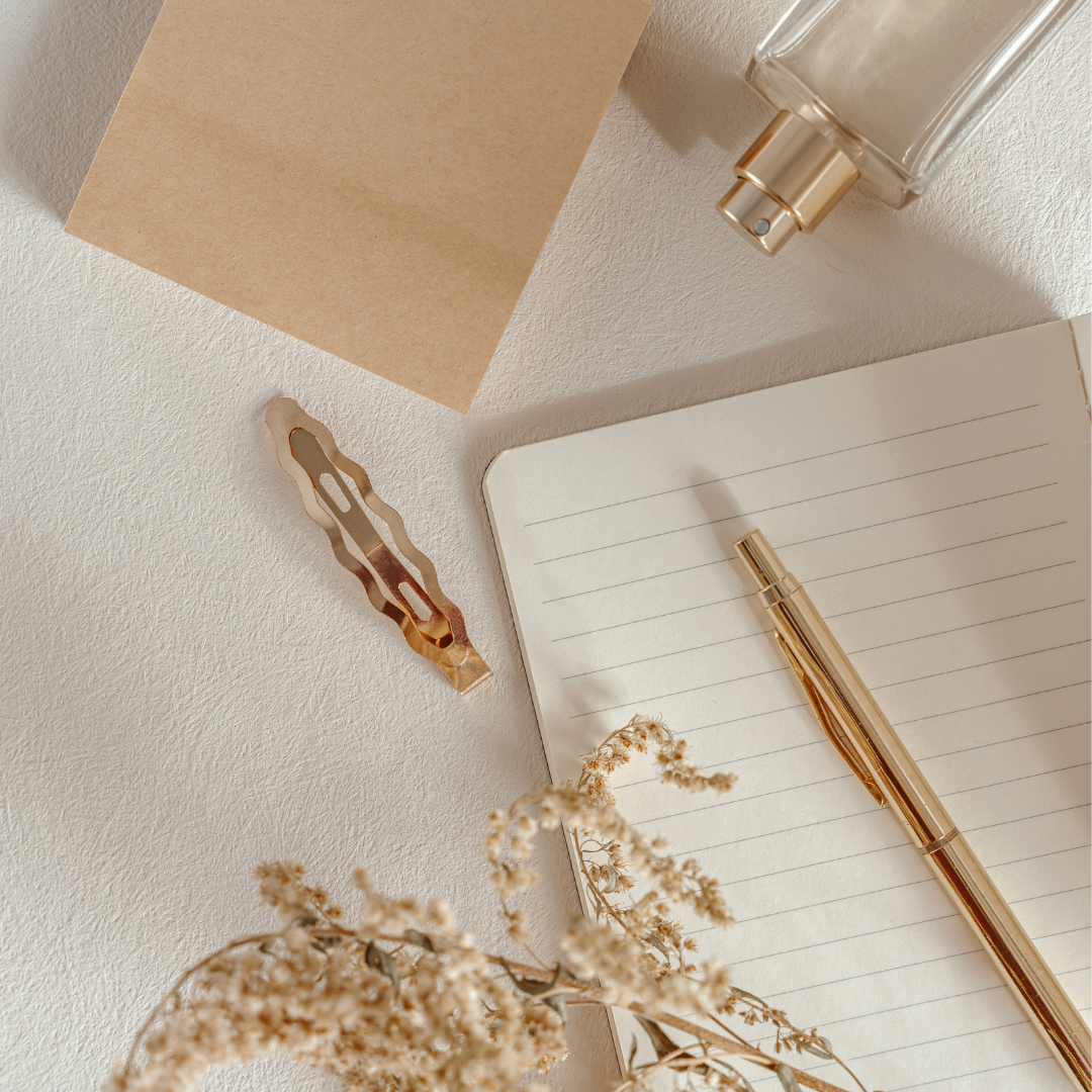 Open notebook with a pen, dried flowers, and a bottle on a light surface